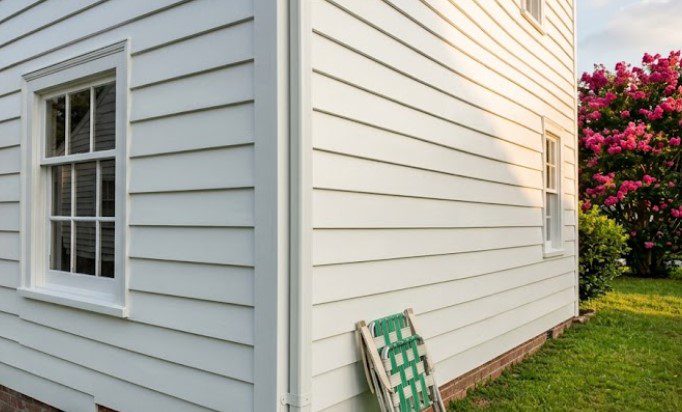 Freshly painted exterior wood siding after blister repair in Hampton Roads, showing window, downspout, and folding chair