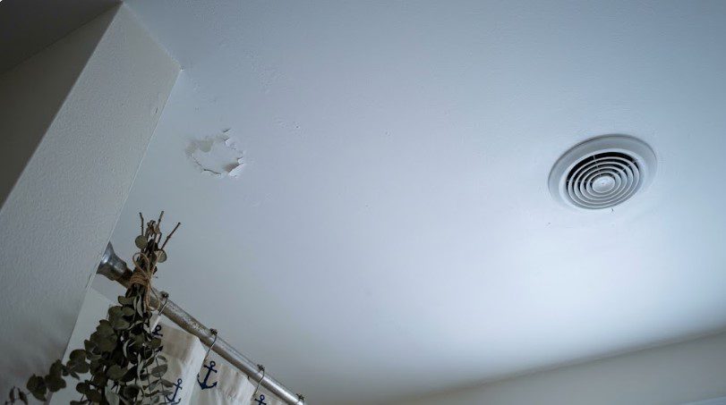 Small patch of paint peeling on a white bathroom ceiling near the shower rod and a round exhaust vent