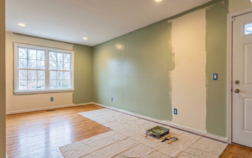 Living room half-painted sage green over cream, with bare winter trees outside the window