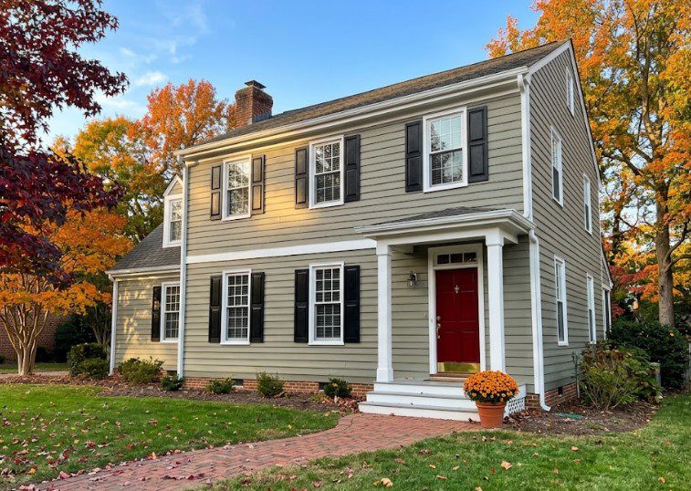 Freshly painted gray-green colonial with black shutters and a red door, surrounded by autumn trees