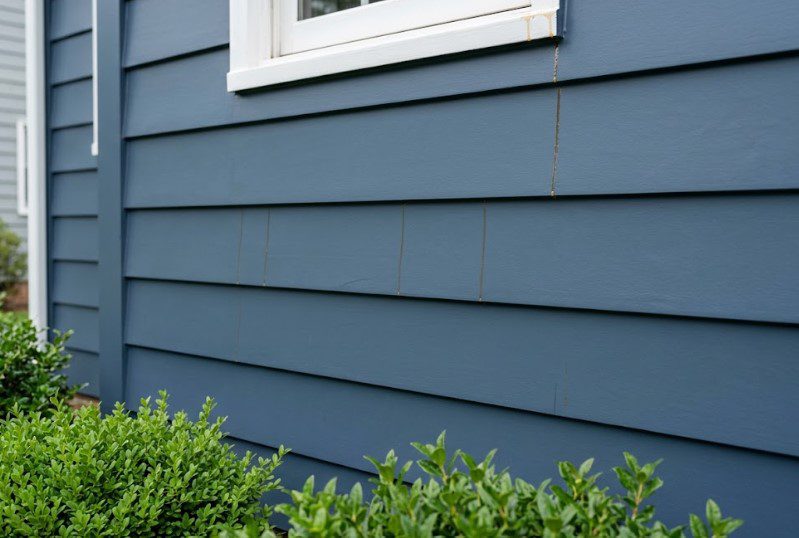 Light brown streaks running down the joints of freshly painted blue siding after a humid night